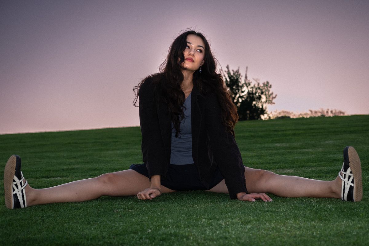 Woman doing a full split on green grass at sunset, city skyline glowing in the distance