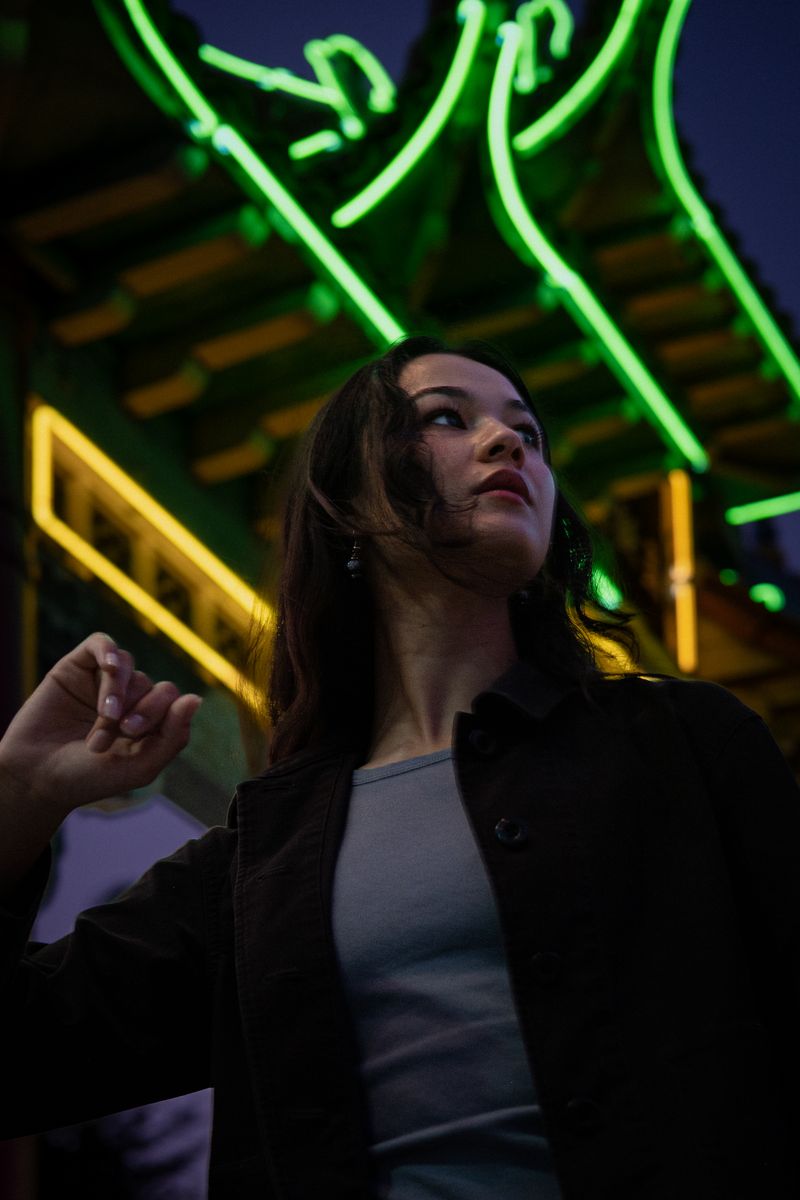 Woman posing beneath glowing green neon signage