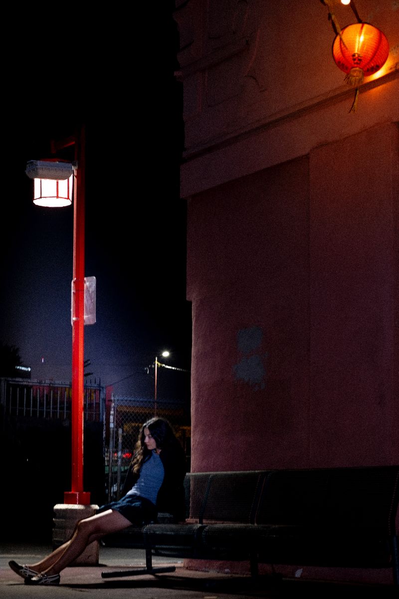 Woman sitting on steps lit by a red lantern against a brick wall at night