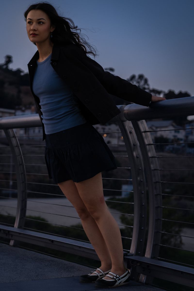 Woman leaning against a railing with the Los Angeles skyline silhouetted behind her at dusk