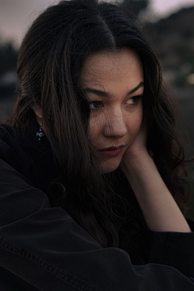 Close-up portrait of a woman resting her chin on her hand in moody blue dusk light