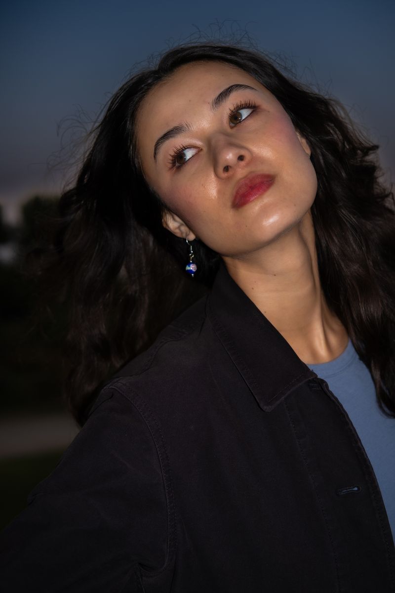 Portrait of a woman with wavy dark hair, softly lit against the evening sky