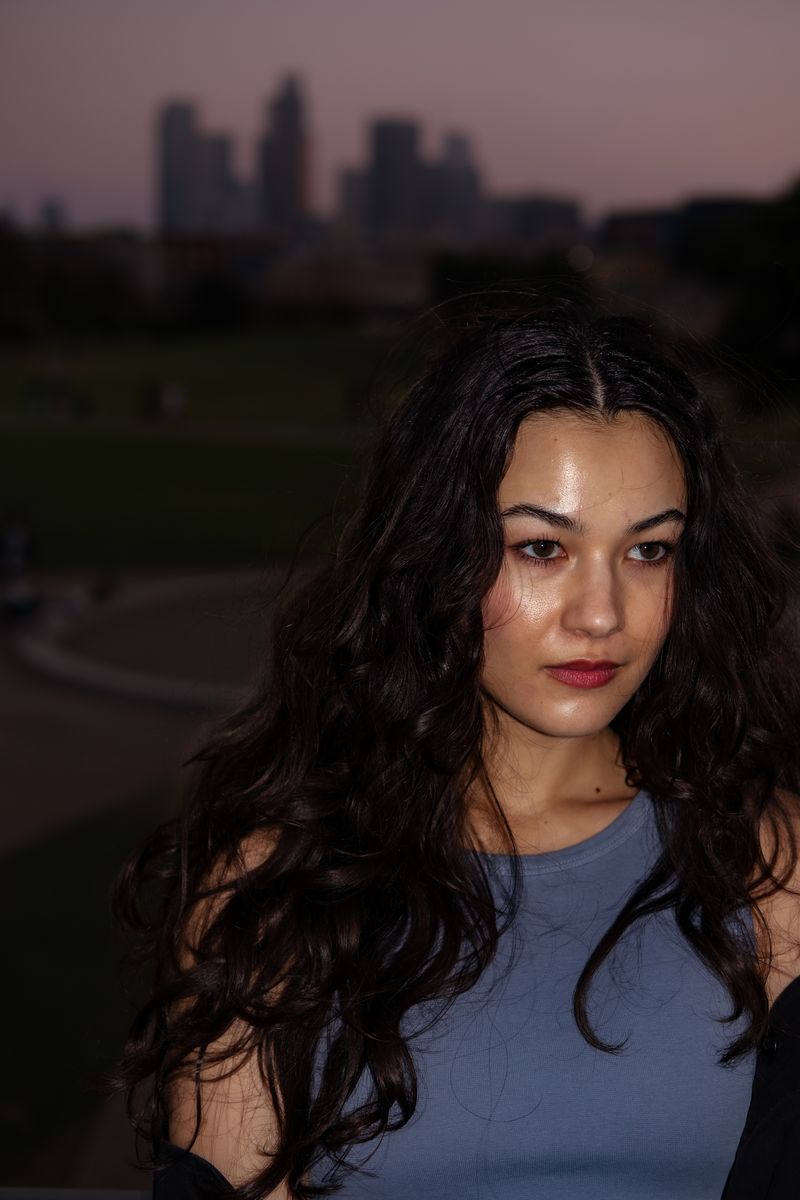 Woman standing with the downtown Los Angeles skyline glowing behind her at dusk