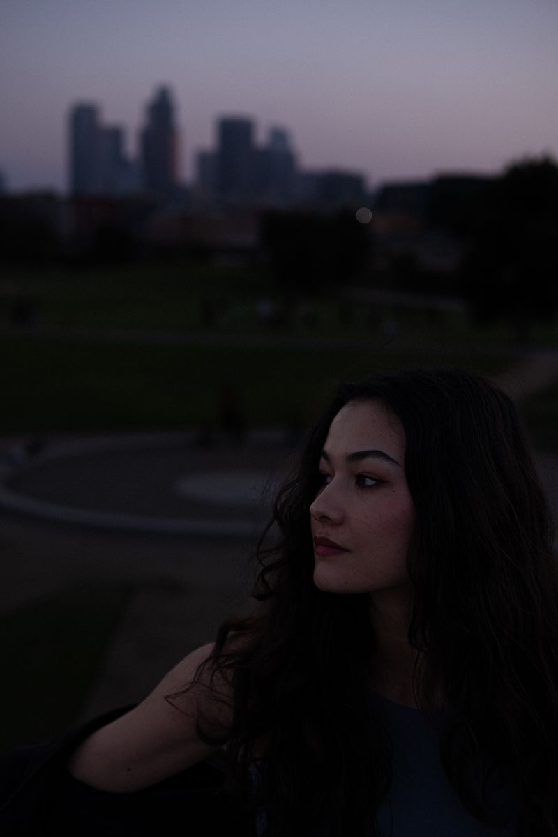 Woman standing in a park with the city skyline behind her, hair blowing gently