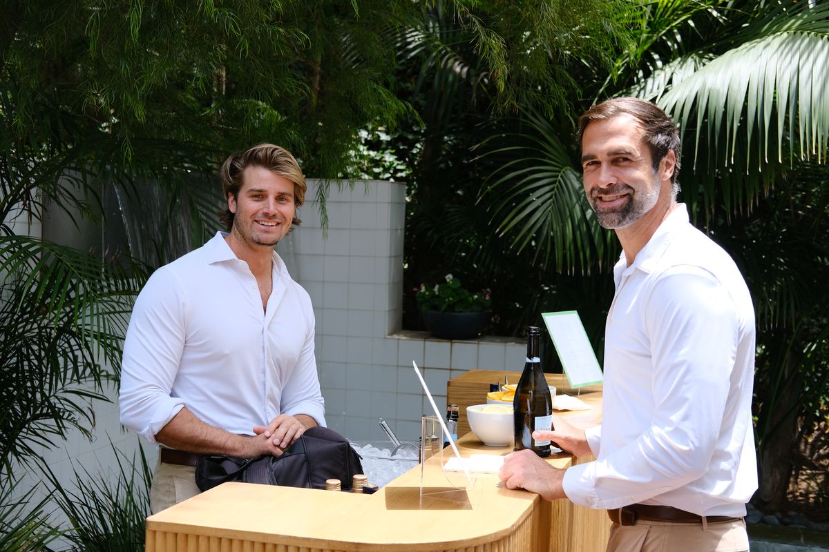 Two men in white shirts talking at an outdoor bar