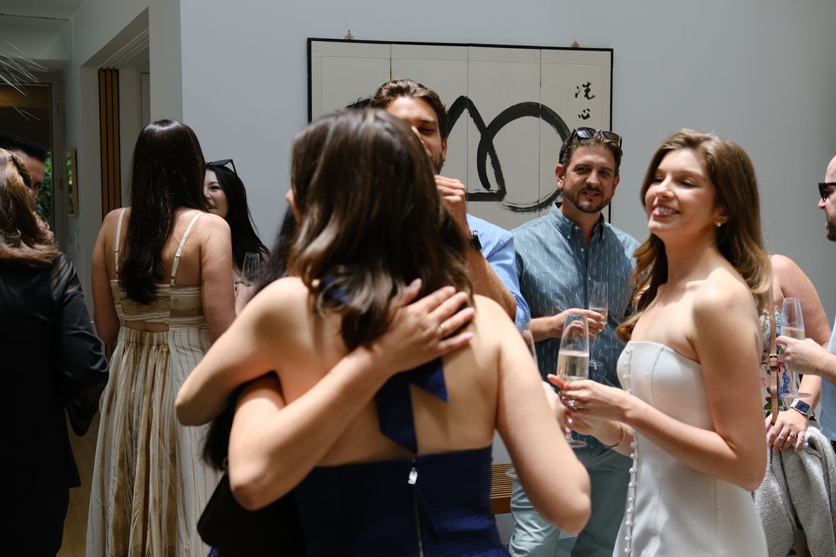 A group of women laughing together, one in a white dress