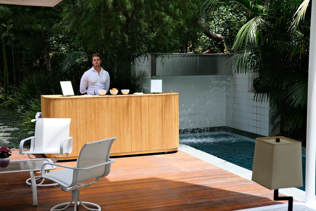 A bartender behind a wooden bar cart beside a pool