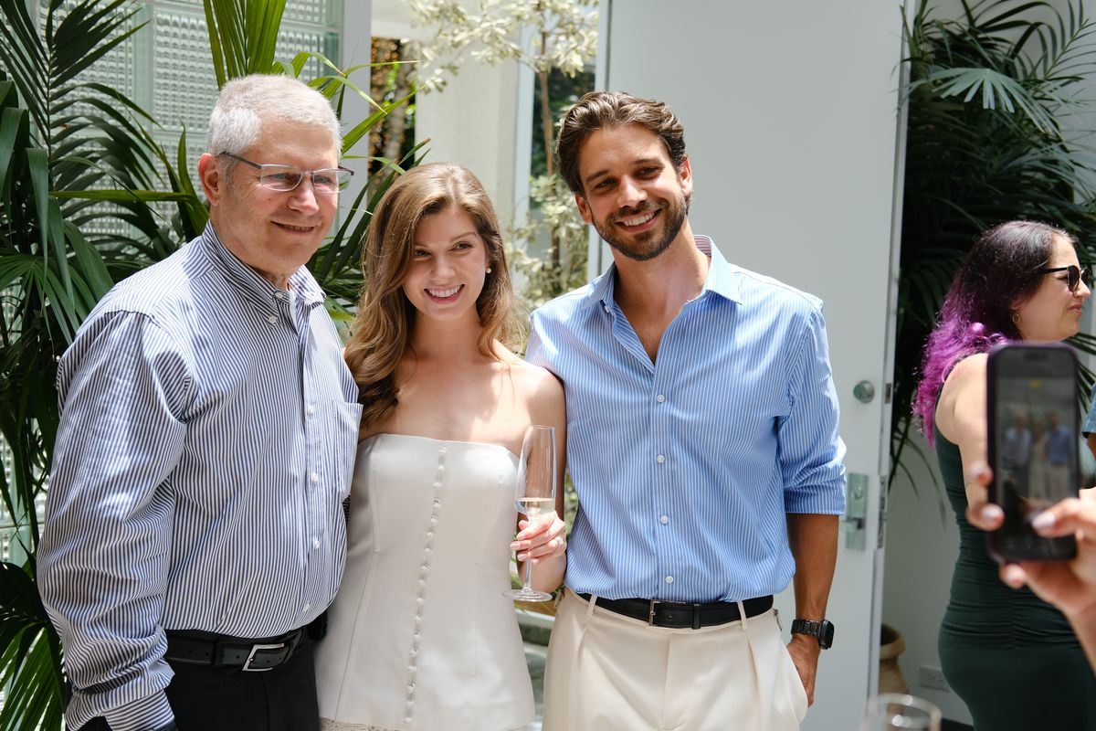 A woman in a white dress standing between two men, smiling for a photo