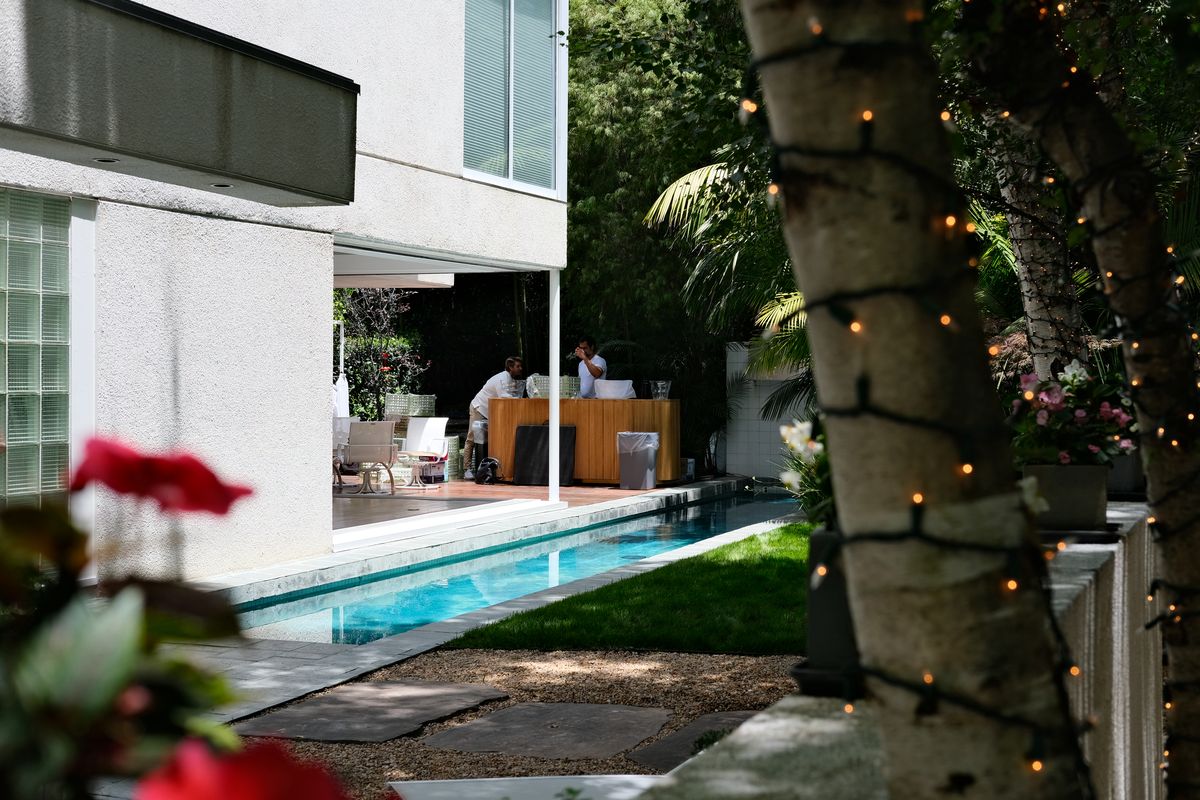 An empty backyard pool and garden strung with lights ahead of a party
