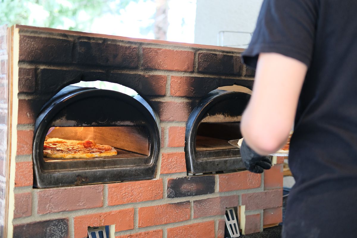 A chef sliding a pizza into a wood-fired brick oven