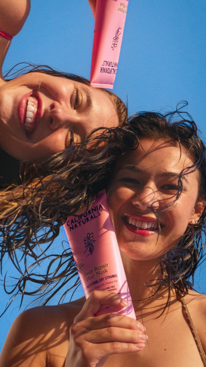 Two women laughing on a beach holding California Naturals product tubes