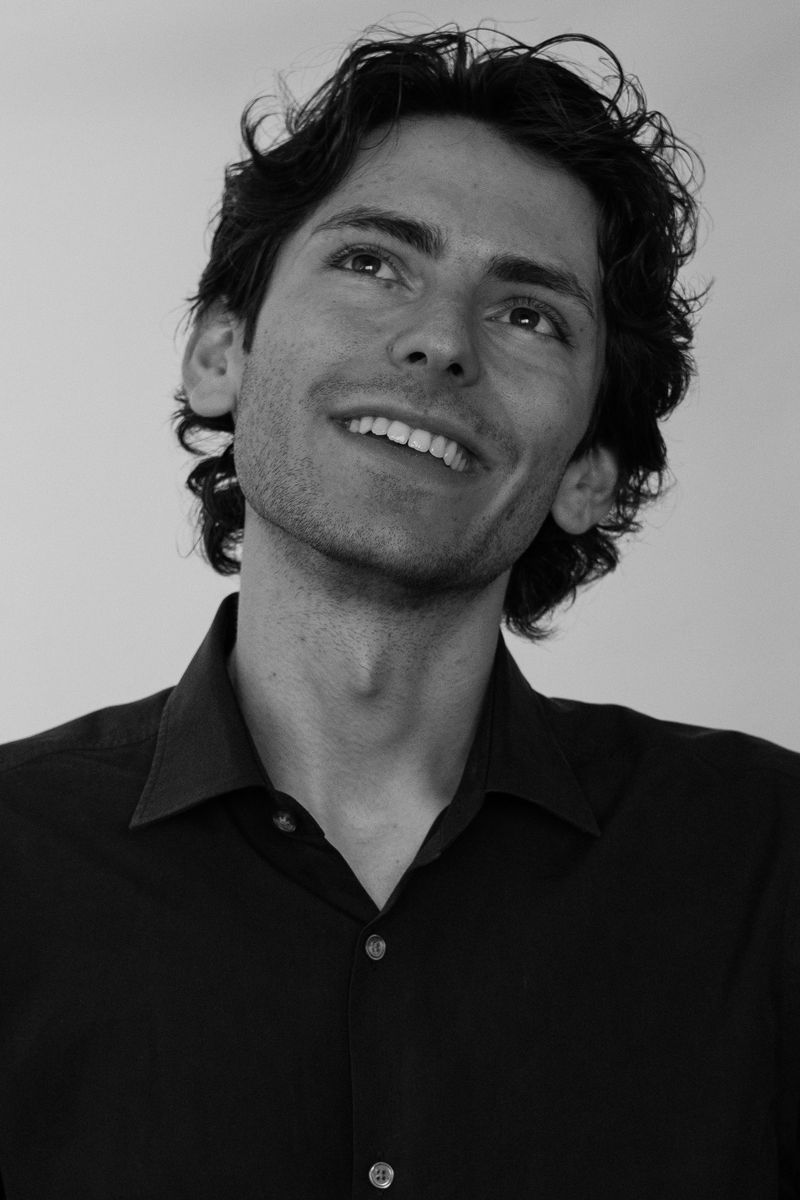 Black-and-white portrait of a man smiling and looking upward against a studio backdrop