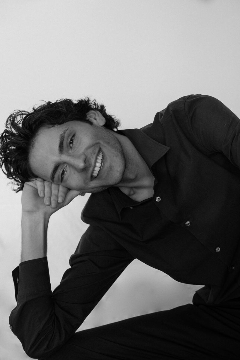 Black-and-white portrait of a man resting his head on his hand, smiling
