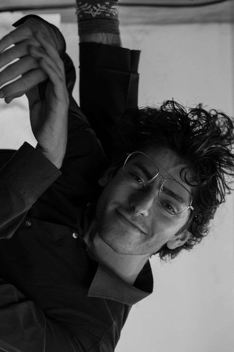 Black-and-white portrait of a man tilting his head back, hand raised beside his face, windblown hair
