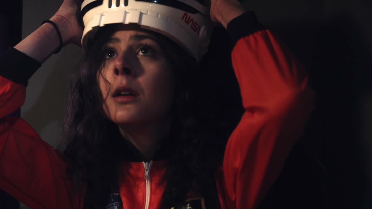 Close-up of a woman in a red flight suit putting on a white astronaut helmet, lit in dramatic red and dark tones, a still from Chinese Satellite